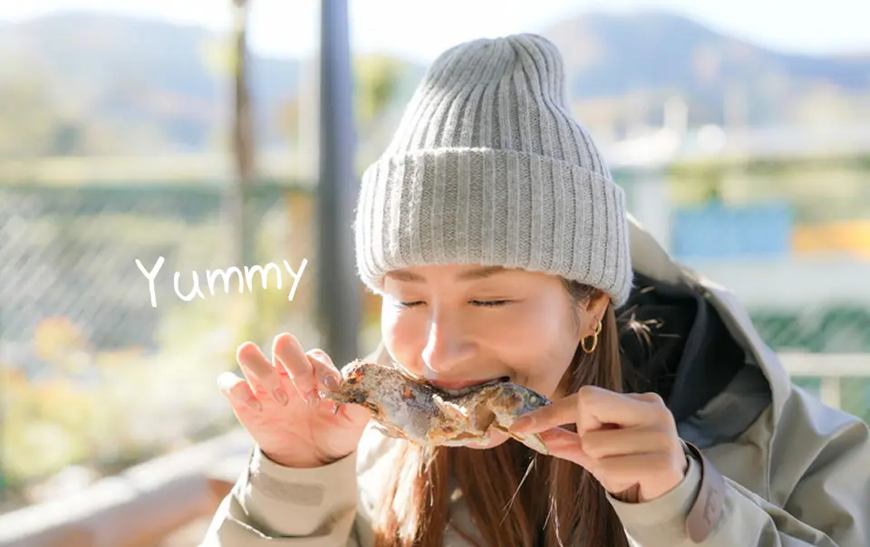 マスの塩焼きを両手で持って食べる女性。Yummy