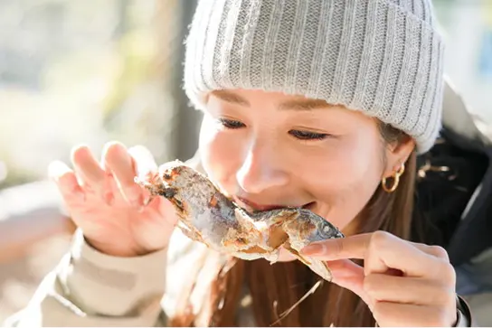 マスの塩焼きを美味しそうに頬張る女性